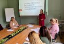 Kobieta w bordowym garniturze prowadzi prezentację dla grupy osób siedzących przy dużym stole konferencyjnym. Na ekranie za nią widnieje napis: „ZADANIA PEDAGOGA SZKOLNEGO W OPRACOWYWANIU OCENY FUNKCJONALNEJ”.